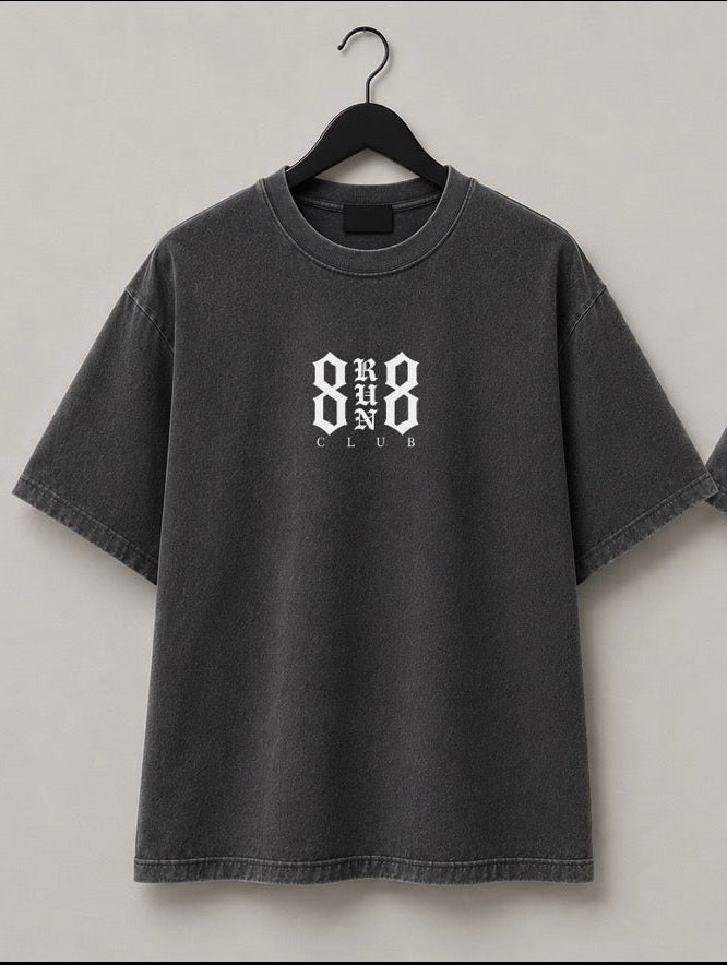 Two views of a dark gray washed t-shirt hanging on black hangers against a light gray wall. The front view shows a small white '888 CLUB' logo on the left chest, and the back view shows a large white '888 RUN CLUB' graphic.