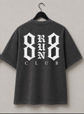 Two views of a dark gray washed t-shirt hanging on black hangers against a light gray wall. The front view shows a small white '888 CLUB' logo on the left chest, and the back view shows a large white '888 RUN CLUB' graphic.