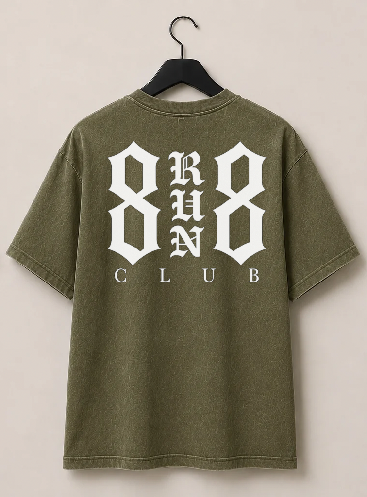 An olive green short-sleeve t-shirt shown from both front and back, hanging on black hangers against a light beige wall. The front features a small white graphic on the left chest, and the back features a large white graphic reading '8 RUN 8 CLUB'.